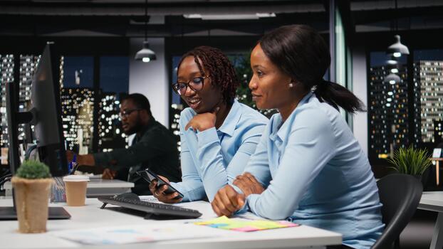 Black women working together with data insights on desktop in workspace, developing business solutions with strategy planning and performance metrics analysis for new goals achievement. photo