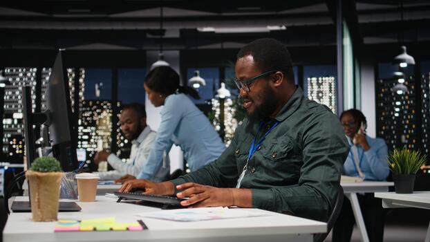 Black male consultant focused on IT company development with digital tools, review analytics and performance metrics at workstation. Staff planning solutions and aligning objectives. photo