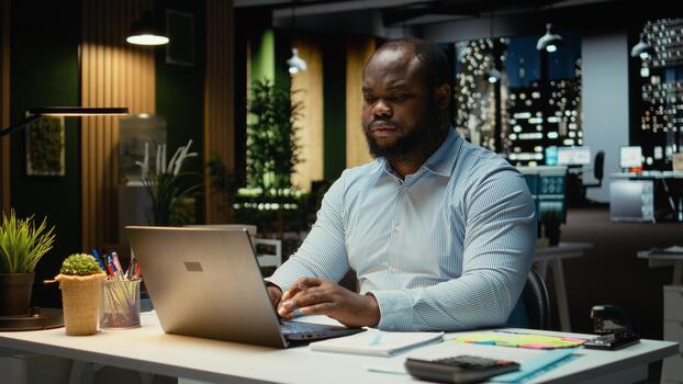 African american analyst pondering about possible outcomes for a problem at workstation after hours, intense concentration to evaluate projections with logical deduction and observation. photo