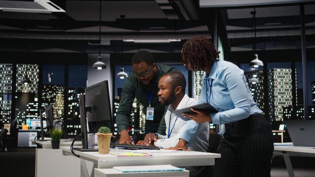 Group of black employees doing teamwork on important task late at night, collaborating on building a new development strategy after hours. Reviewing insights to enhance efficiency. photo
