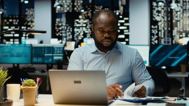Black business consultant working after hours fact checking web information, writing important data on laptop. Creating a summary and designing strategy to align with enterprise targets. photo