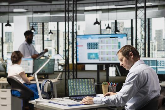 Male analyst in office examines stock trading data on digital device, comparing with information from clipboard. Businessman uses laptop to analyze forex market and reviews index charts on documents. photo