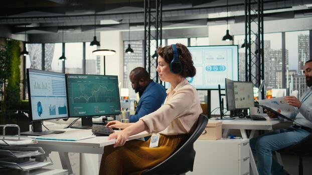 Office administrator uses focus music on headset to solve tasks, monitoring performance metrics at the workstation. Administrative tasks to ensure enterprise productivity and success. photo