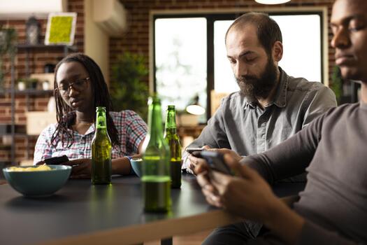 caucásico masculino individual usos Teléfono móvil a vistazo en línea, con cerveza botella metido en mesa en frente de a él. barbado blanco hombre con móvil dispositivo, se sienta en medio de amigos, disfrutando su compañía. foto