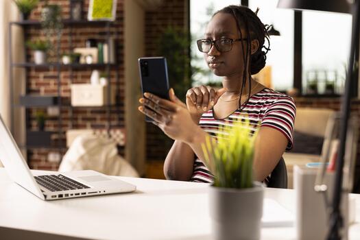 Self employed woman holds phone during remote team meeting, reviewing performance metrics in home office. Focused entrepreneur on call via smartphone, discussing company data and operations. photo