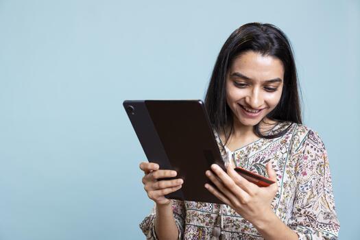 Indian woman enjoying online shopping on her tablet in front of the camera, adding payment credentials on the website. Smiling girl buying stuff online using credit card, typing data on device. photo