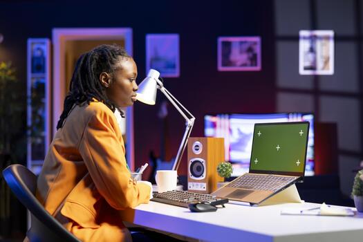 Worker at home office desk browsing internet on mockup laptop, researching information online. Woman using search engines on green screen notebook to find data relevant to work tasks, reading articles photo