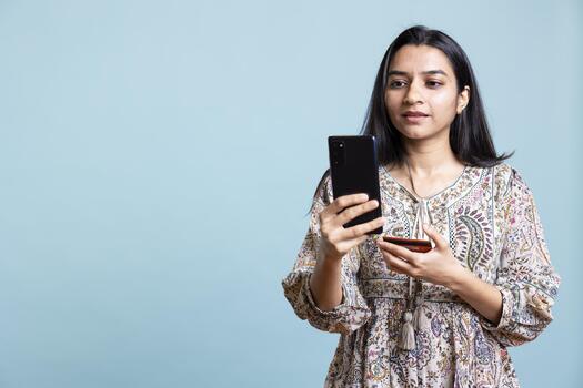 Indian woman excited to purchase stuff adding payment method on website with her smartphone, isolated over studio background. Ecstatic client does internet shopping, typing debit card info. photo