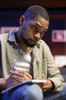 Focused person manages research by taking notes from online articles, working remotely on the couch at home. Freelancer multitasking and studying data driven papers, collect info. photo