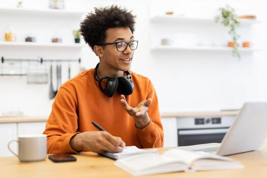 A young man with glasses is engaged in a call, taking notes on a notepad while working from home. photo