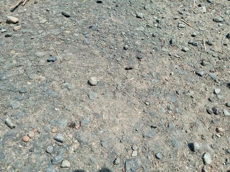 Closeup Texture of Rough Asphalt Road Surface with Small Stones and Dust in Sunlight photo