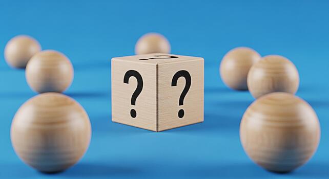 Wooden cube displaying question marks surrounded by wooden spheres on a blue surface representing uncertainty mystery and the search for answers in a minimalist and conceptual composition photo