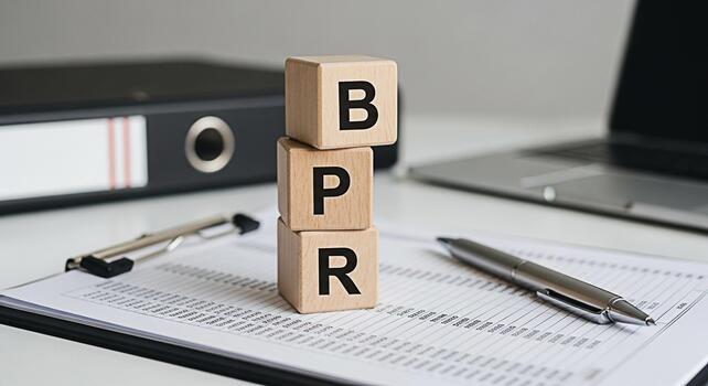 Wooden blocks spelling BPR on a clipboard in a bright office setting symbolizing Business Process Reengineering and efficiency with a laptop and binder in the background conveying a concept of corpora photo