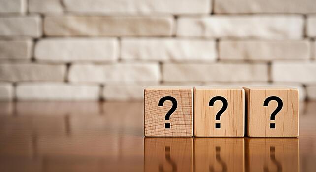 Three wooden blocks displaying question marks sit on a reflective wooden surface against a blurred brick wall representing uncertainty inquiry and the search for answers in a conceptual setting photo