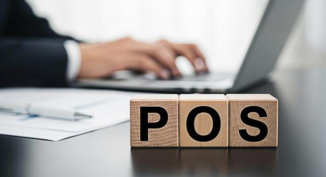 Unrecognizable businessman typing on a laptop in a modern office with wooden blocks spelling POS symbolizing point of sale systems and efficient business transactions conveying a professional and tech photo
