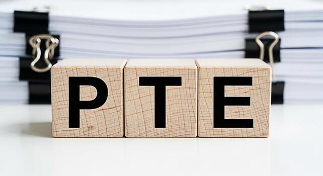 Wooden blocks displaying PTE letters on a white desk with stacked papers symbolizing preparation for the Pearson Test of English and promoting education and language proficiency photo
