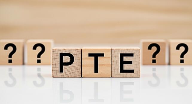 Wooden blocks spelling PTE on a white surface surrounded by question marks representing the Pearson Test of English and the uncertainty of exam preparation in an educational setting photo