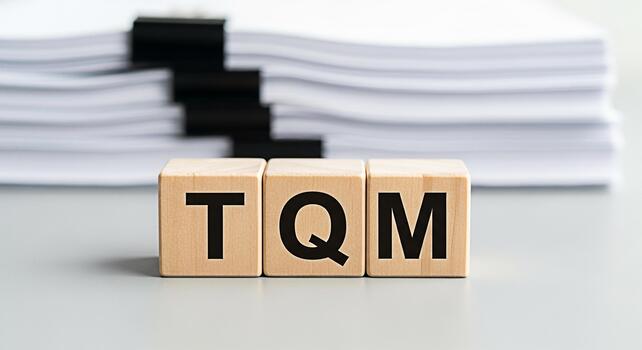 Wooden blocks displaying TQM on a gray surface with a stack of documents emphasizing total quality management in a business setting conveying efficiency organization and process improvement photo