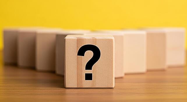 Wooden block displaying a question mark on a wooden table against a bright yellow background representing uncertainty inquiry and the search for answers in a conceptual and minimalist setting photo