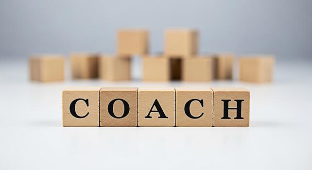 Wooden blocks spelling COACH on a white surface symbolizing guidance and support with a blurred background of additional blocks creating a sense of depth and focus on the coaching concept photo