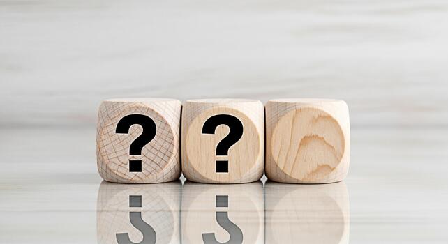Three wooden dice displaying question marks on a reflective surface symbolizing uncertainty and the need for answers in a bright clean studio environment evoking curiosity and problemsolving photo