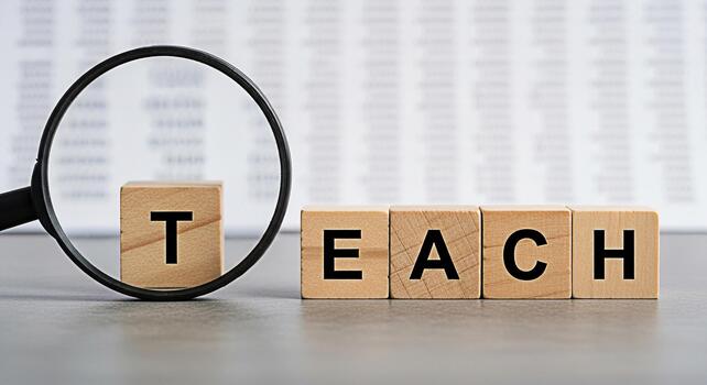 Magnifying glass focusing on the word TEACH spelled out with wooden blocks on a gray surface symbolizing education learning and the importance of knowledge in a classroom setting photo