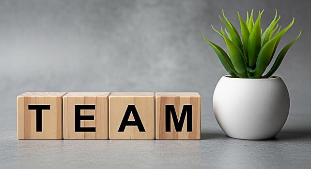 de madera bloques ortografía equipo desplegado en un gris superficie siguiente a un pequeño en conserva planta simbolizando colaboración y unidad en un moderno minimalista espacio de trabajo Fomentando un sentido de trabajo en equipo y crecimiento foto