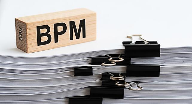 Wooden block displaying BPM on a stack of documents with binder clips in a bright office setting representing business process management and workflow efficiency photo