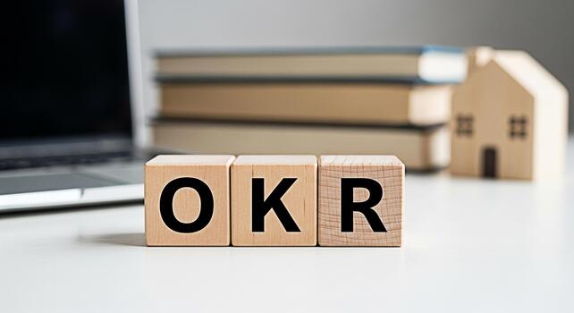 Wooden blocks displaying OKR on a white desk with a laptop and books symbolizing goal setting and achievement in a modern office environment promoting business strategy and objectives key results photo