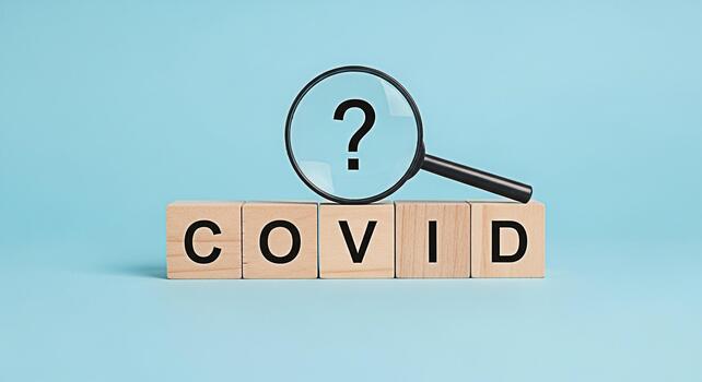 Magnifying glass hovering over wooden blocks spelling COVID with a question mark symbolizing uncertainty and the ongoing search for answers in a light blue studio setting creating a sense of concern photo