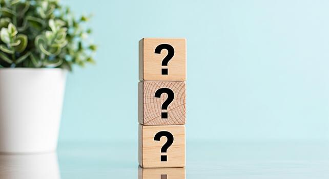 Stacked wooden blocks displaying question marks in a bright studio setting symbolizing uncertainty and the search for answers with a clean minimalist aesthetic and a potted plant accent photo