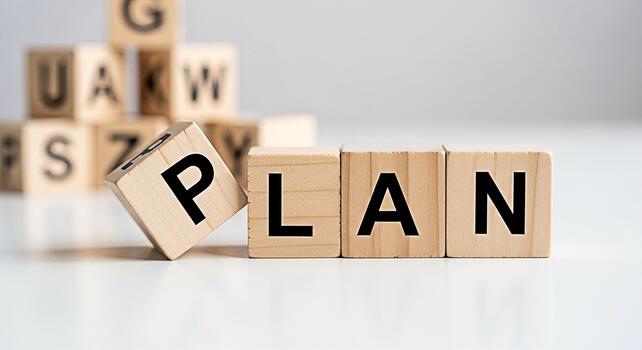Wooden blocks spelling PLAN on a white surface with a pyramid of lettered blocks in the background symbolizing strategic planning and business development in a minimalist setting conveying a sense of photo
