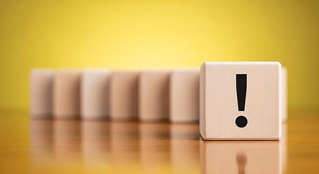 Wooden block displaying an exclamation mark stands out from the row on a yellow background symbolizing attention warning or important information in a simple and minimalist design conveying a sense of photo