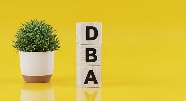 Wooden blocks displaying DBA acronym next to a potted plant against a vibrant yellow background representing database administration and business operations with a clean and modern aesthetic photo