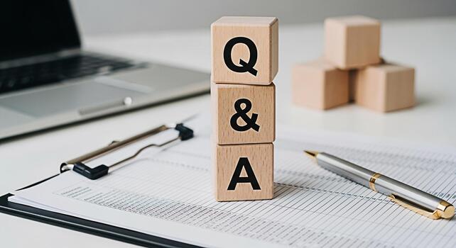 Wooden blocks displaying QA on a bright white desk with a laptop clipboard and pen representing information support and answers to questions in a professional and informative setting photo