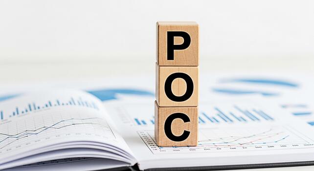 Wooden blocks spelling POC resting on an open financial report in a bright office symbolizing proof of concept and strategic business planning for successful project implementation and market validati photo