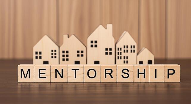 Wooden blocks spelling Mentorship stand in front of miniature house models on a wooden surface symbolizing guidance and support in achieving homeownership dreams fostering a sense of community and sec photo