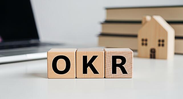 Wooden blocks spelling OKR on a white desk with a laptop and books in the background representing goal setting and objectives and key results for business success and productivity in a modern office photo