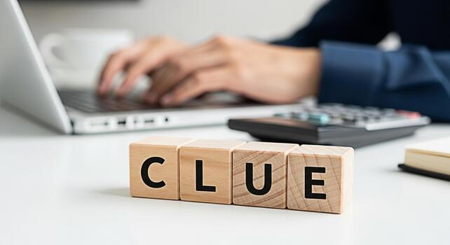 Business professional typing on a laptop in a bright office with wooden blocks spelling CLUE representing problemsolving investigation and the search for answers in a modern workplace environment photo