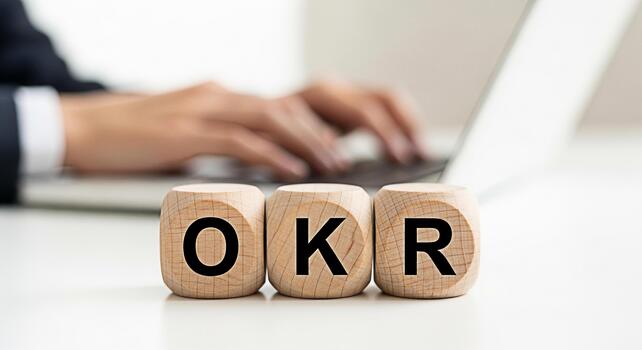 Focused professional typing on a laptop with OKR wooden blocks on a white desk representing objectives and key results for business strategy and goal setting in a modern office environment photo