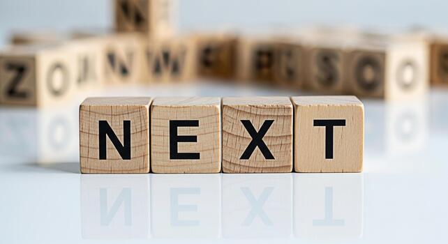 Wooden blocks spelling NEXT on a reflective white surface suggesting anticipation and progress with blurred blocks in the background symbolizing future possibilities and a forwardthinking mindset photo