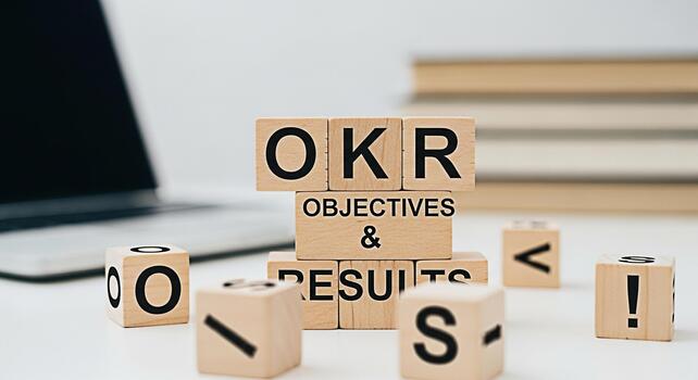 Wooden blocks spelling OKR Objectives and Key Results on a white desk with a laptop and books representing business strategy goal setting and performance management in a modern office environment photo
