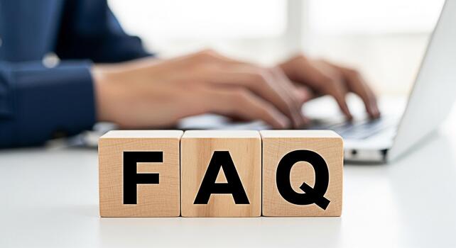 Person typing on a laptop with wooden blocks spelling FAQ on a white desk representing frequently asked questions and seeking information online in a modern office environment photo