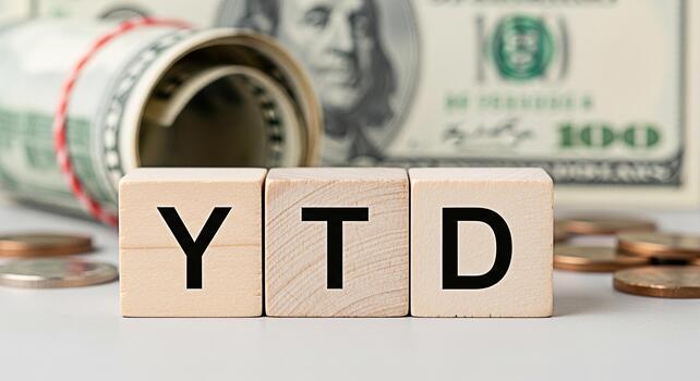 Wooden blocks displaying YTD near rolled US currency and coins representing yeartodate financial performance and investment tracking in a business setting conveying a sense of financial analysis and g photo