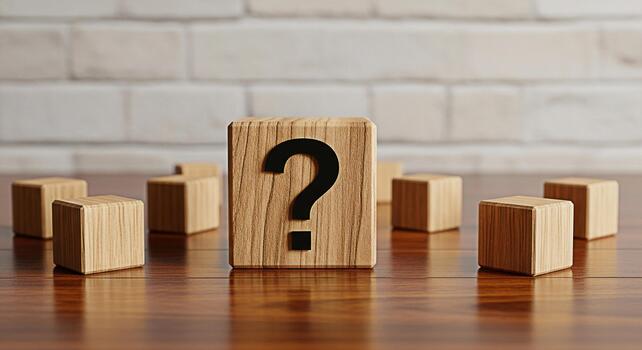 Wooden block displaying a question mark symbol on a shiny wooden surface surrounded by other blocks against a white brick wall representing uncertainty and the search for answers photo