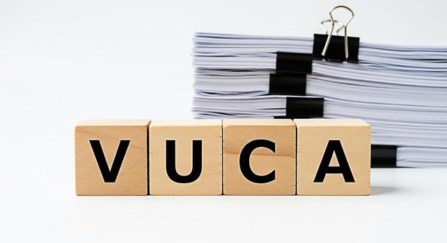 Wooden blocks displaying VUCA acronym representing Volatility Uncertainty Complexity Ambiguity sitting on a white table with a stack of papers symbolizing business challenges and strategic planning photo