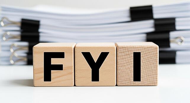Wooden blocks displaying FYI on a white surface with a stack of documents in the background conveying a message of important information and awareness in a professional setting photo