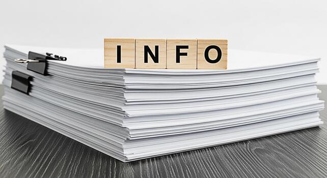 Stack of white papers displaying wooden blocks spelling INFO on a dark wooden desk representing data overload and the need for information management in a modern office environment photo