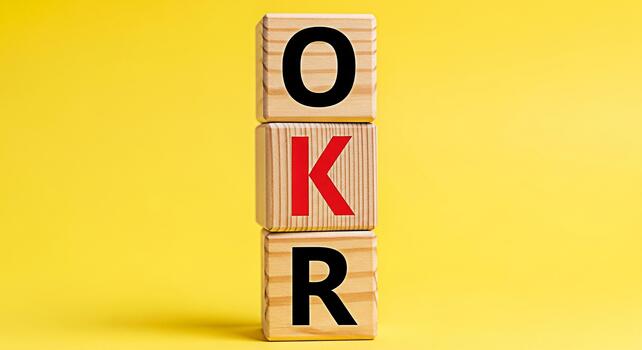 Wooden blocks displaying the acronym OKR standing for Objectives and Key Results in a bright yellow studio setting representing business strategy goal setting and performance management for success photo