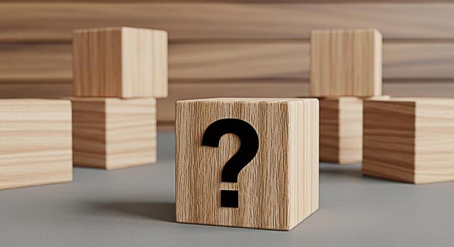 Wooden block displaying a question mark symbol sitting on a gray surface with other blocks in the background representing uncertainty curiosity and the search for answers in a minimalist setting photo